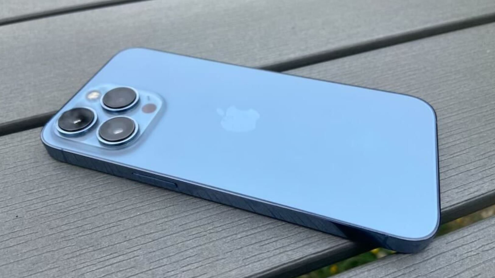 Голубой iPhone 13 Pro лежит на деревянной поверхности