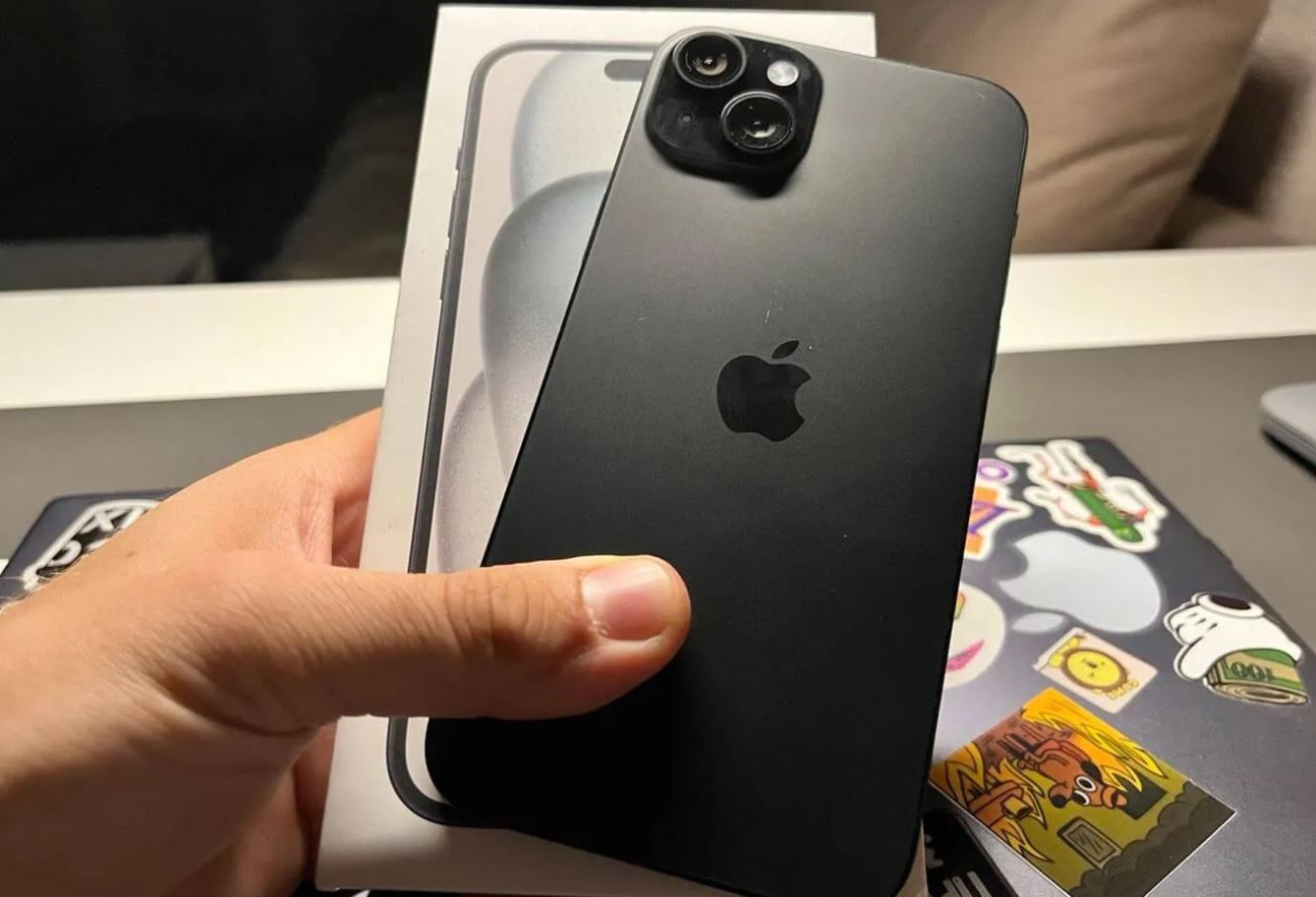 Чёрный iPhone 15 Plus в руке на фоне коробки